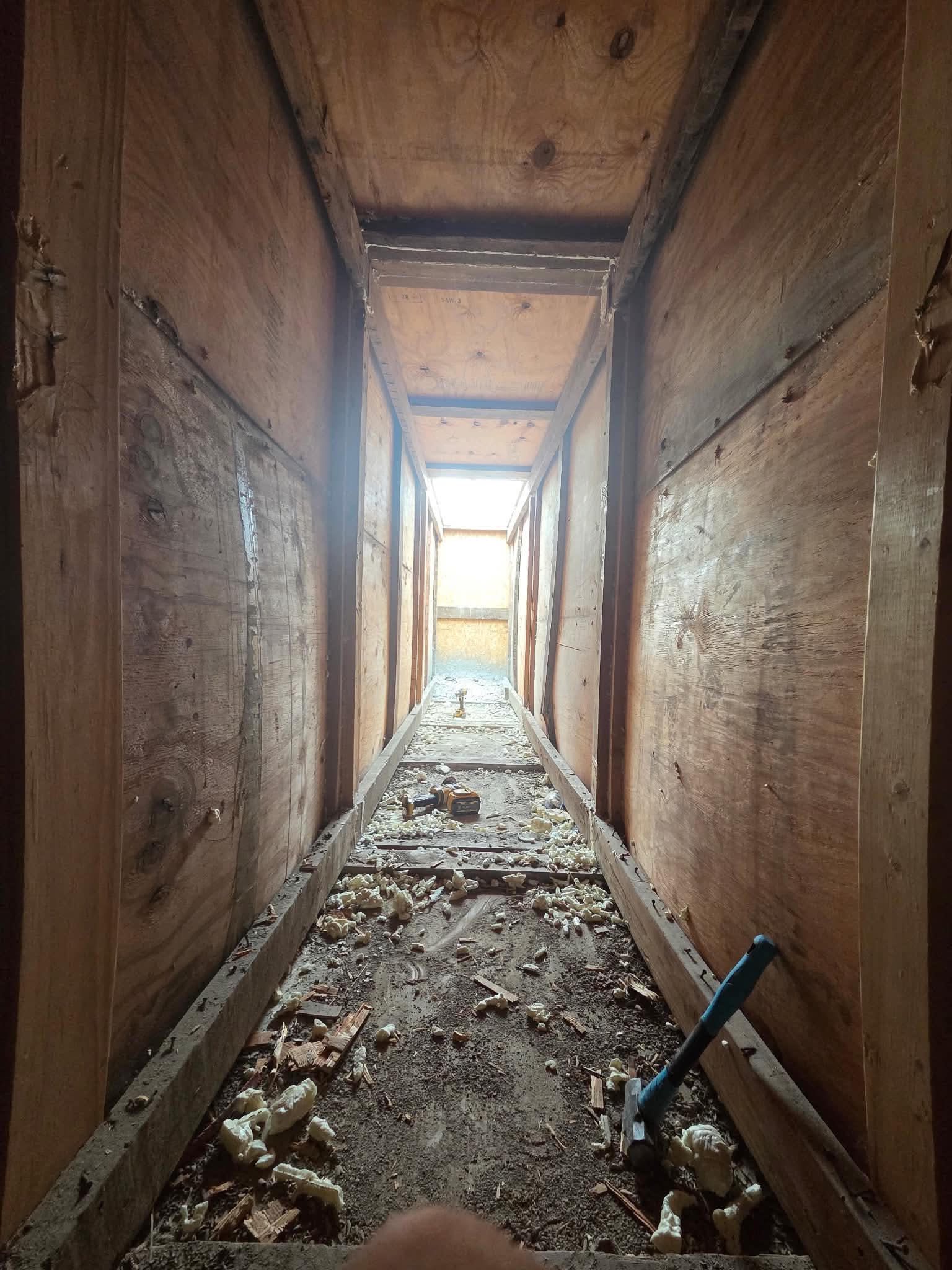 Inside a timber-framed corridor with plywood walls, spray-foam offcuts and tools on the floor
