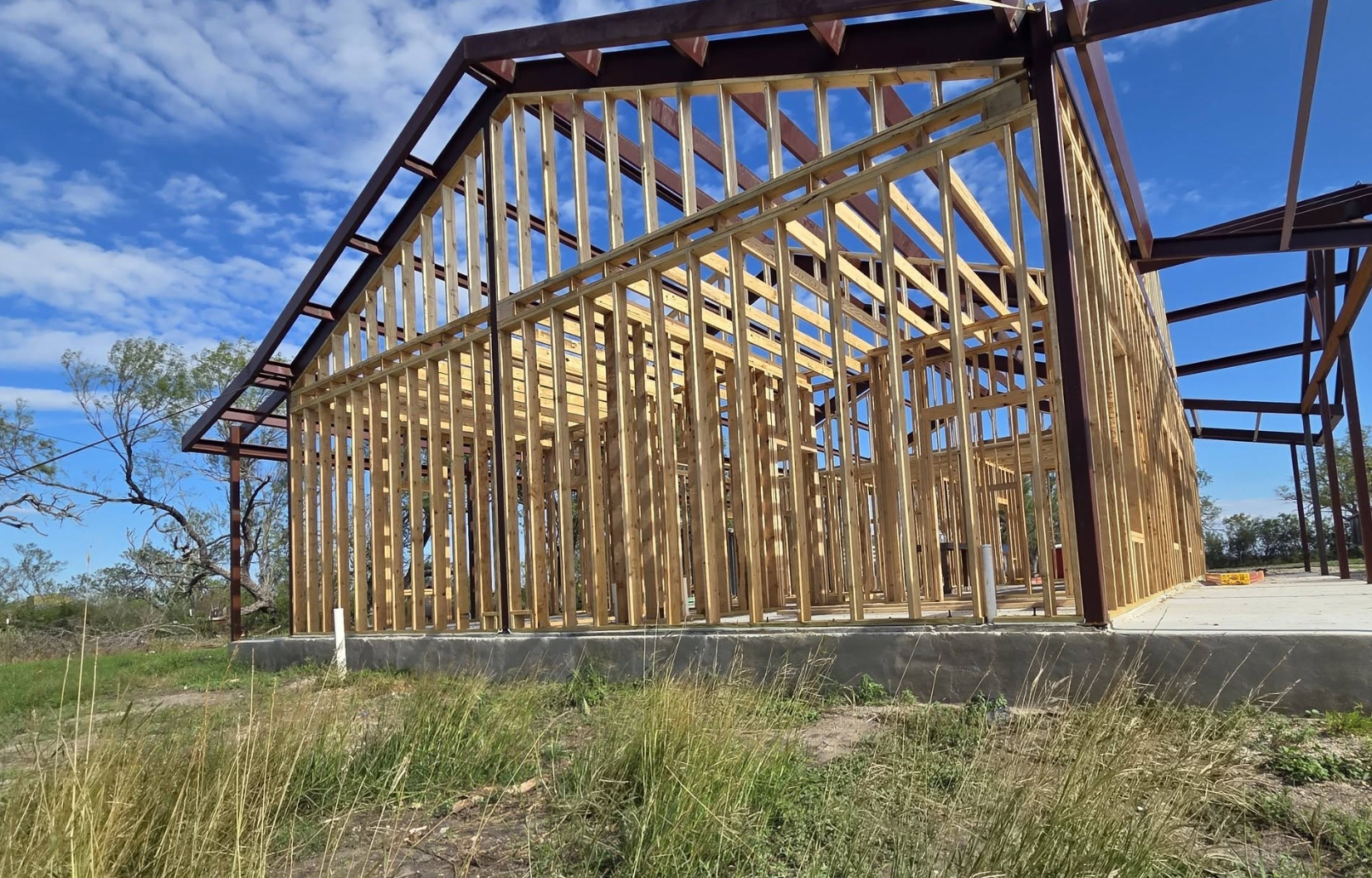 Barndominium under construction — steel portal frame with full wood stud framing on a poured slab under open sky