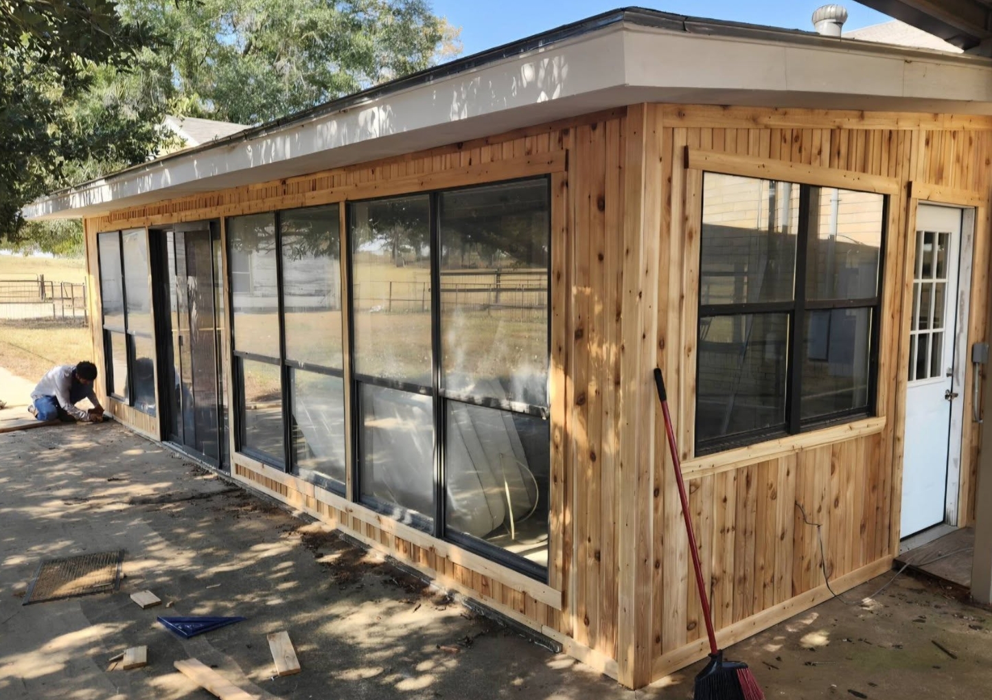 Cedar-clad sunroom enclosure with black-framed windows under construction