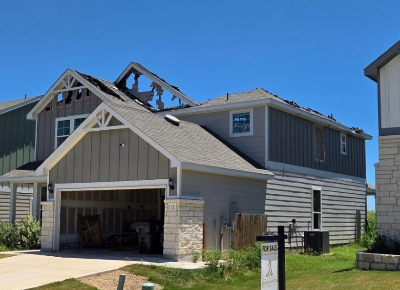 Two-storey home with its roof burned through — charred rafters and holes open to the sky above the gables